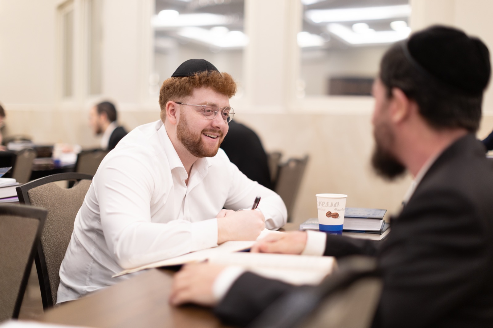 A smiling talmid learning with a rebbi at the yeshiva