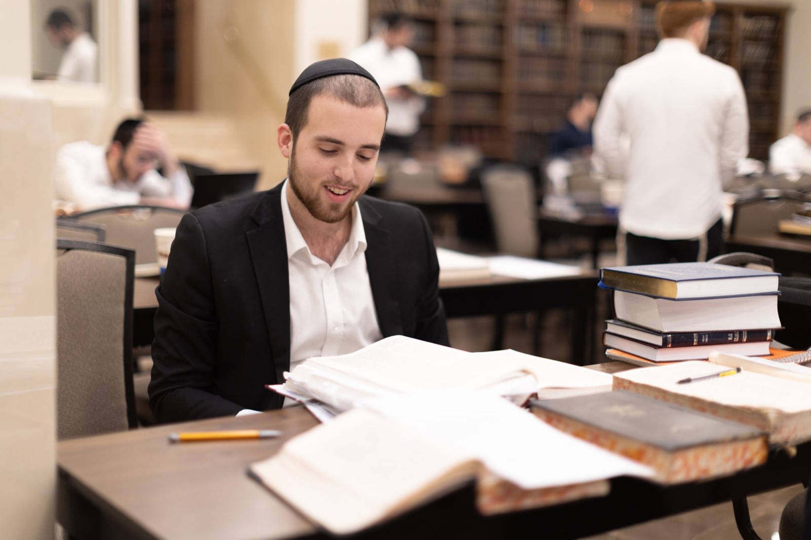 A smiling talmid learning with open sefarim in the beis medrash